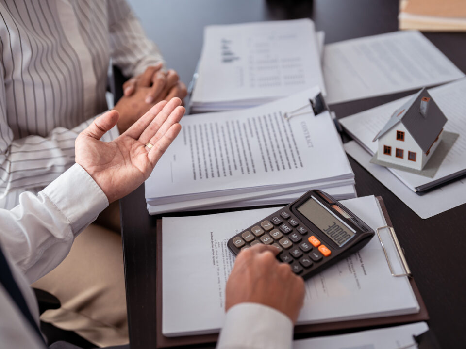Businessman real estate seller calculating about property investment and showing statistic on calculator while discuss to explaining terms data of home sales contract and home insurance for customer