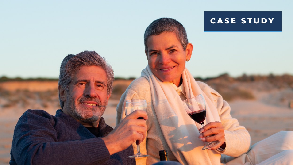 Smiling older couple raising glasses of wine on a beach at sunset